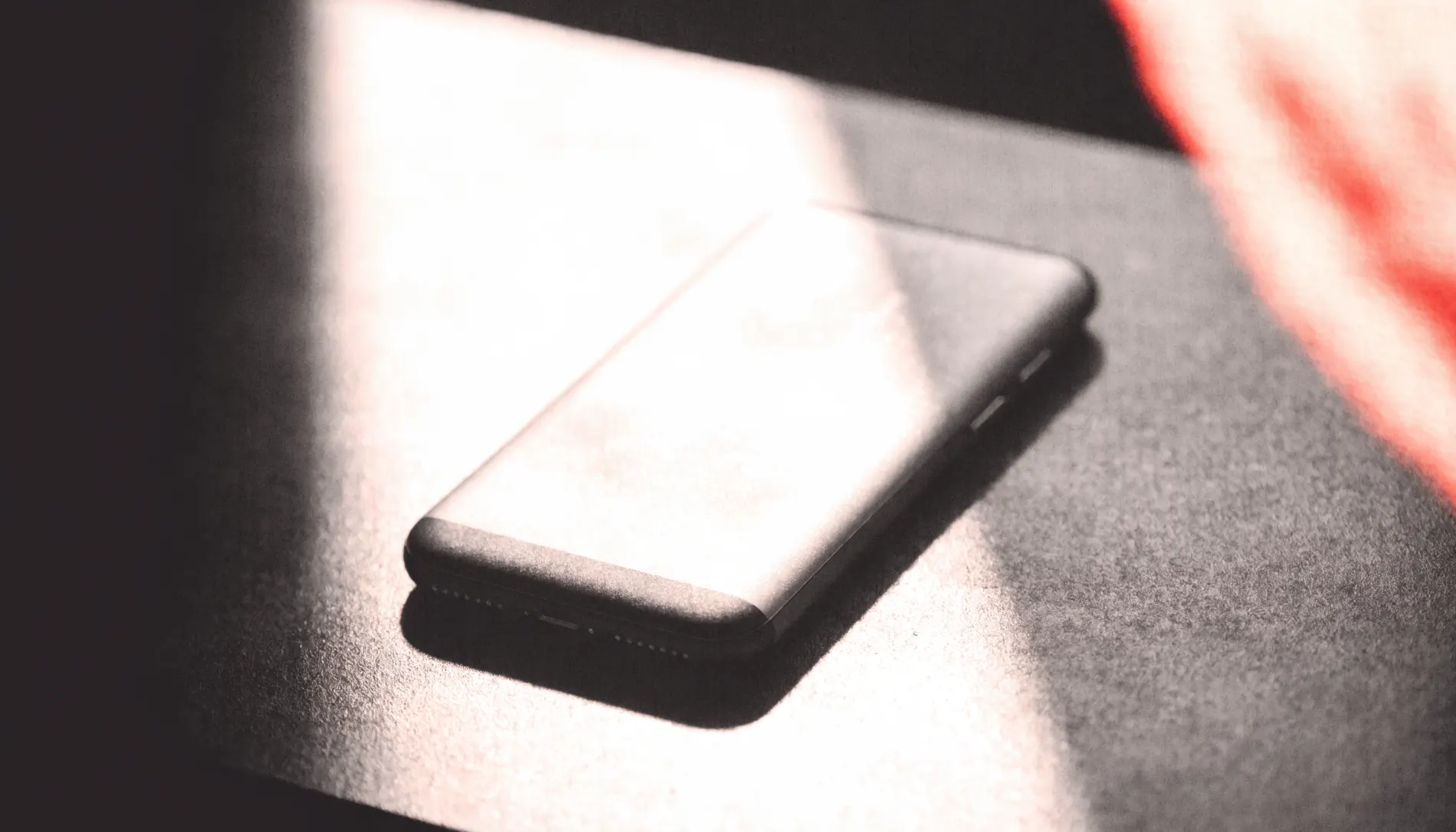 A phone lying face down under a hard shadow