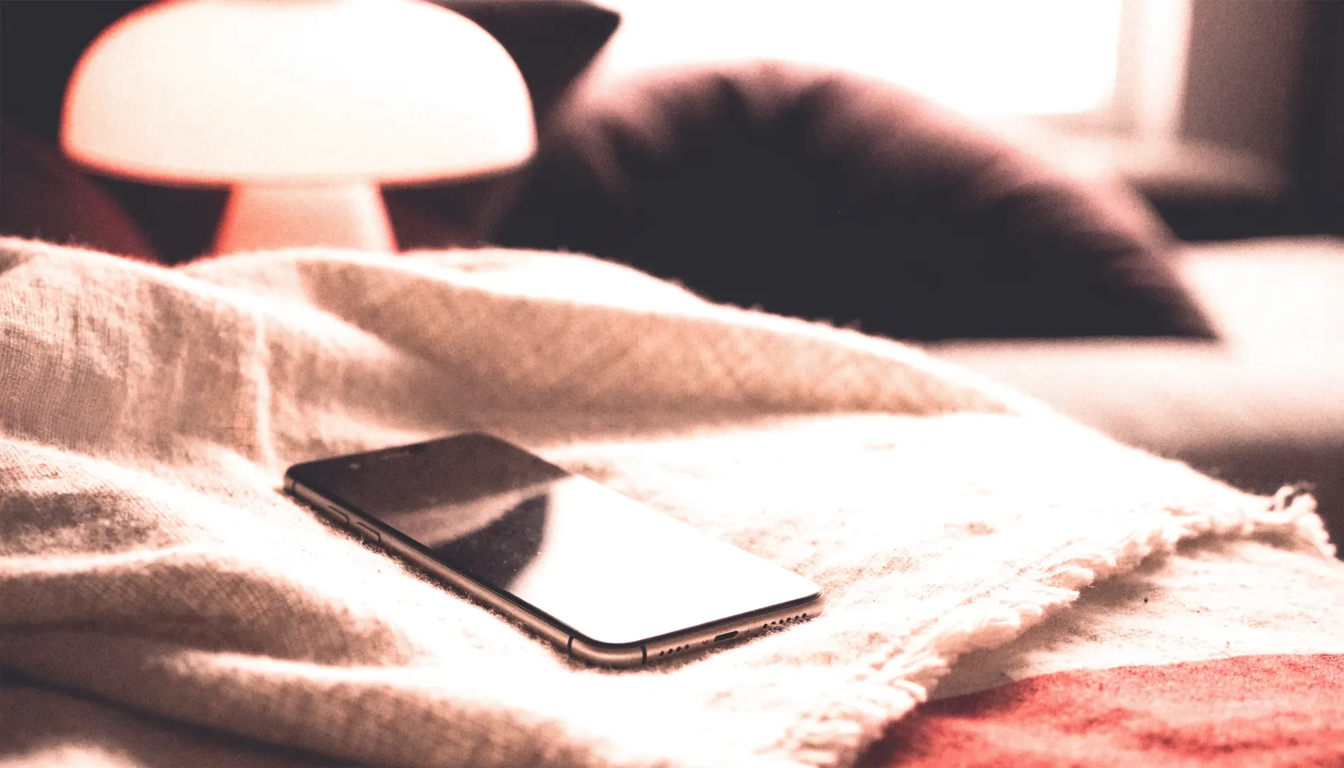 A phone resting on a folded blanket in warm lamplight