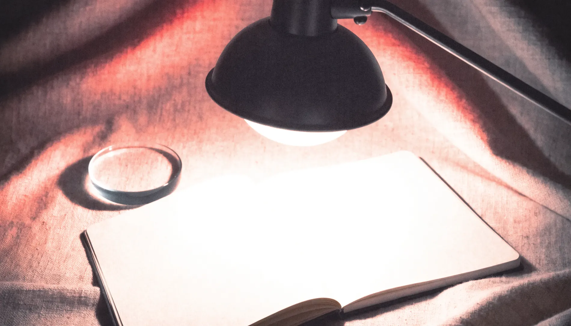 A desk lamp over an open notebook and a glass lens