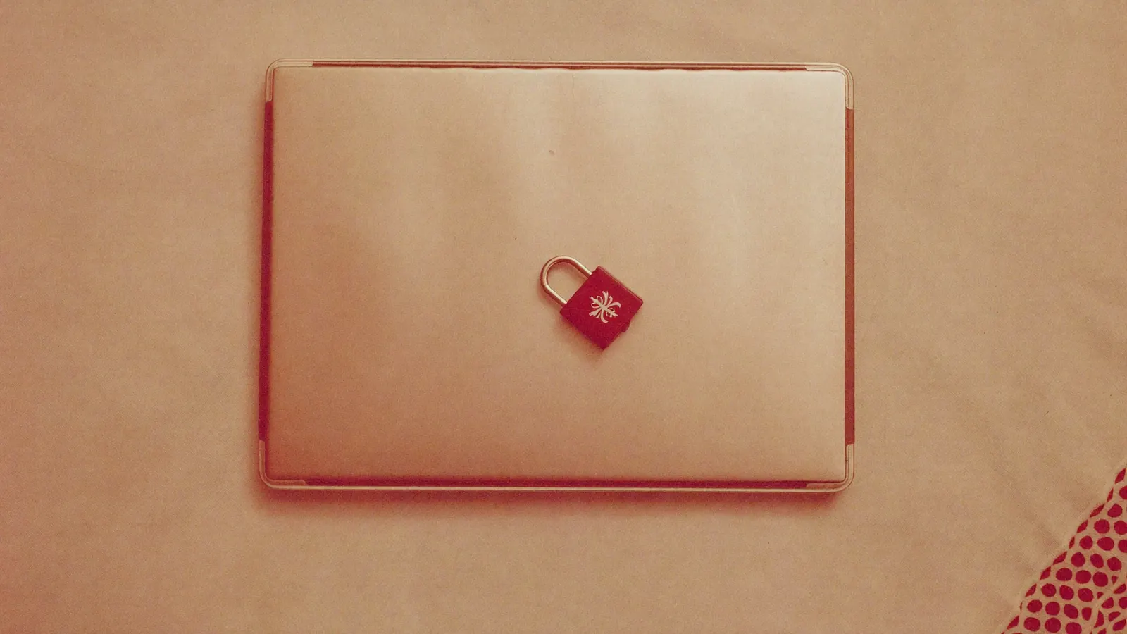 A closed laptop with a small padlock resting on it on a linen tablecloth