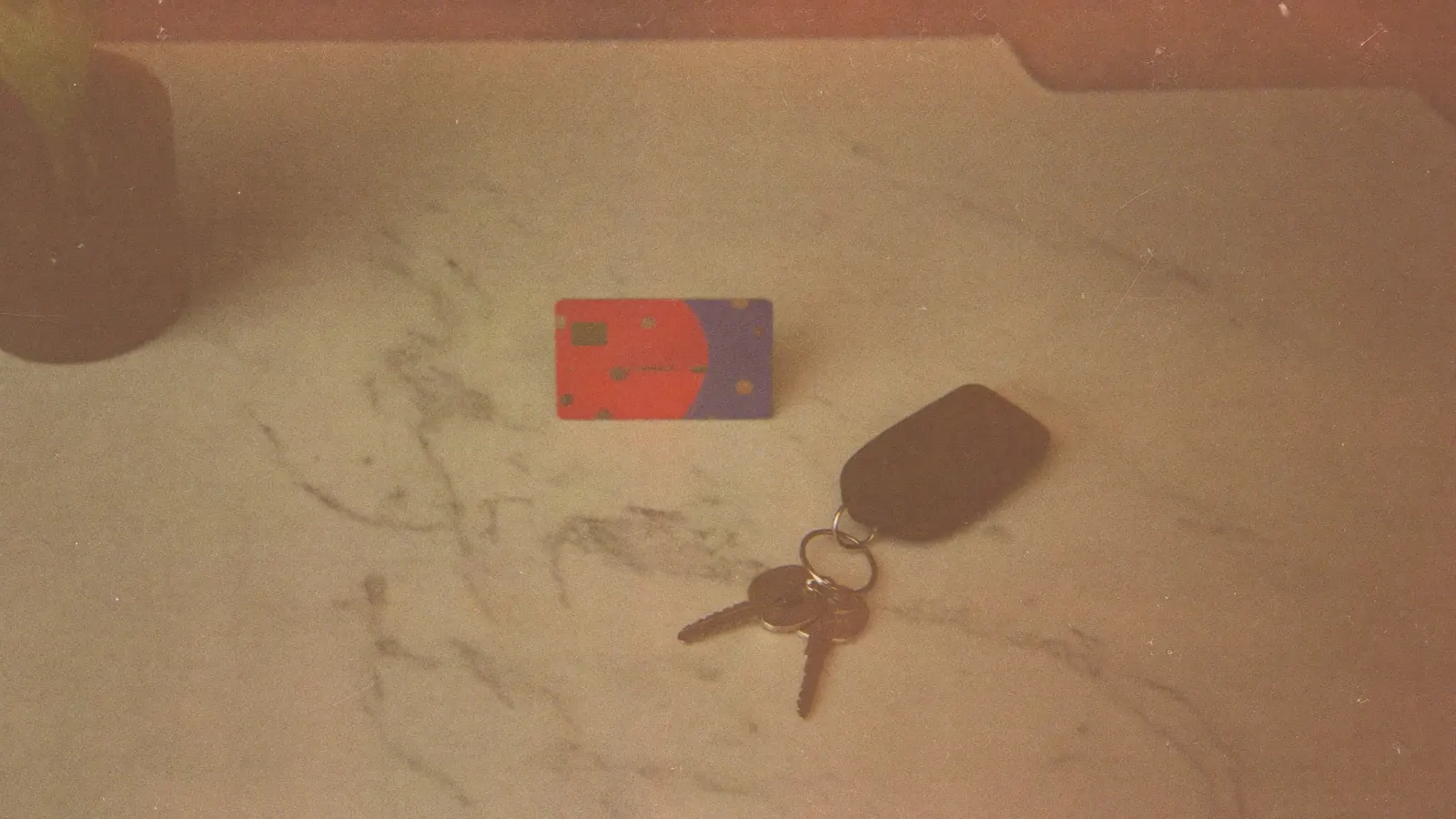 A credit card and car keys on a marble kitchen counter beside a small plant