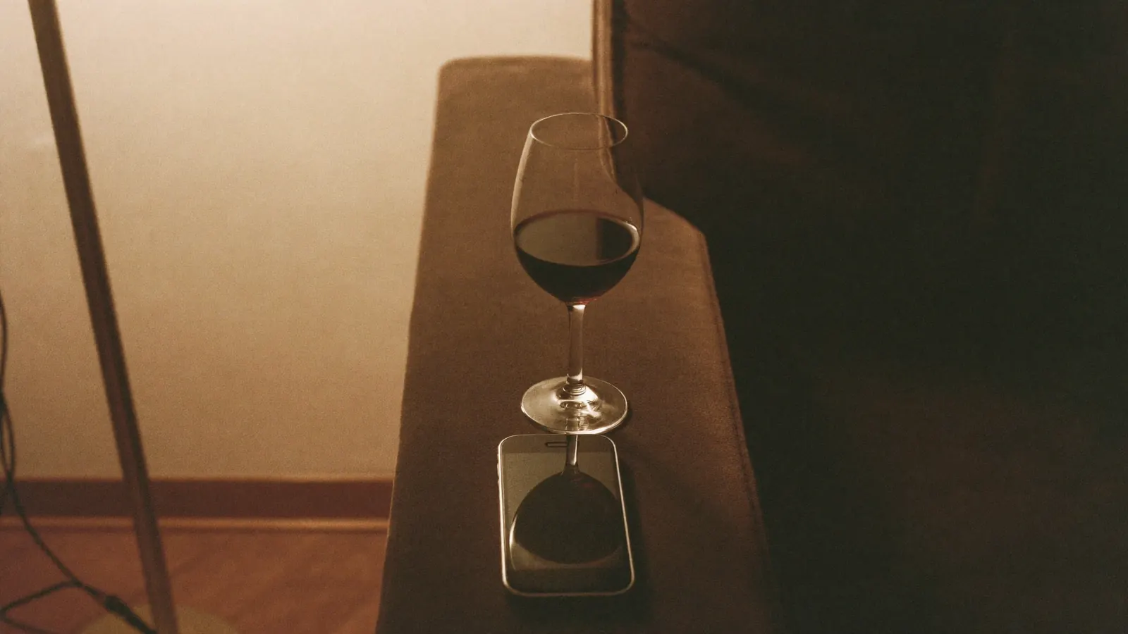 A glass of red wine and a phone on a velvet sofa arm