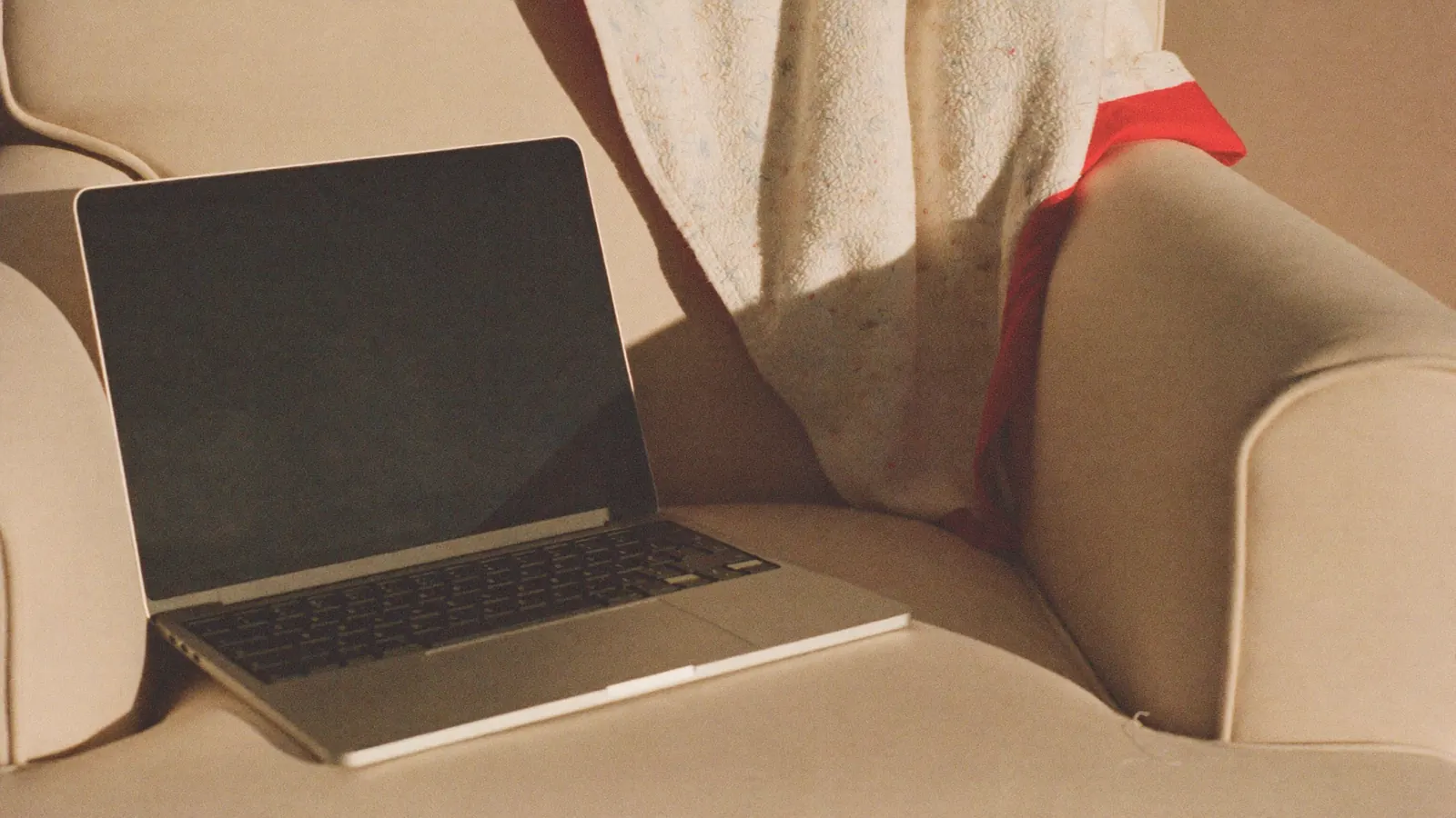 A laptop on a cream armchair with a red scarf