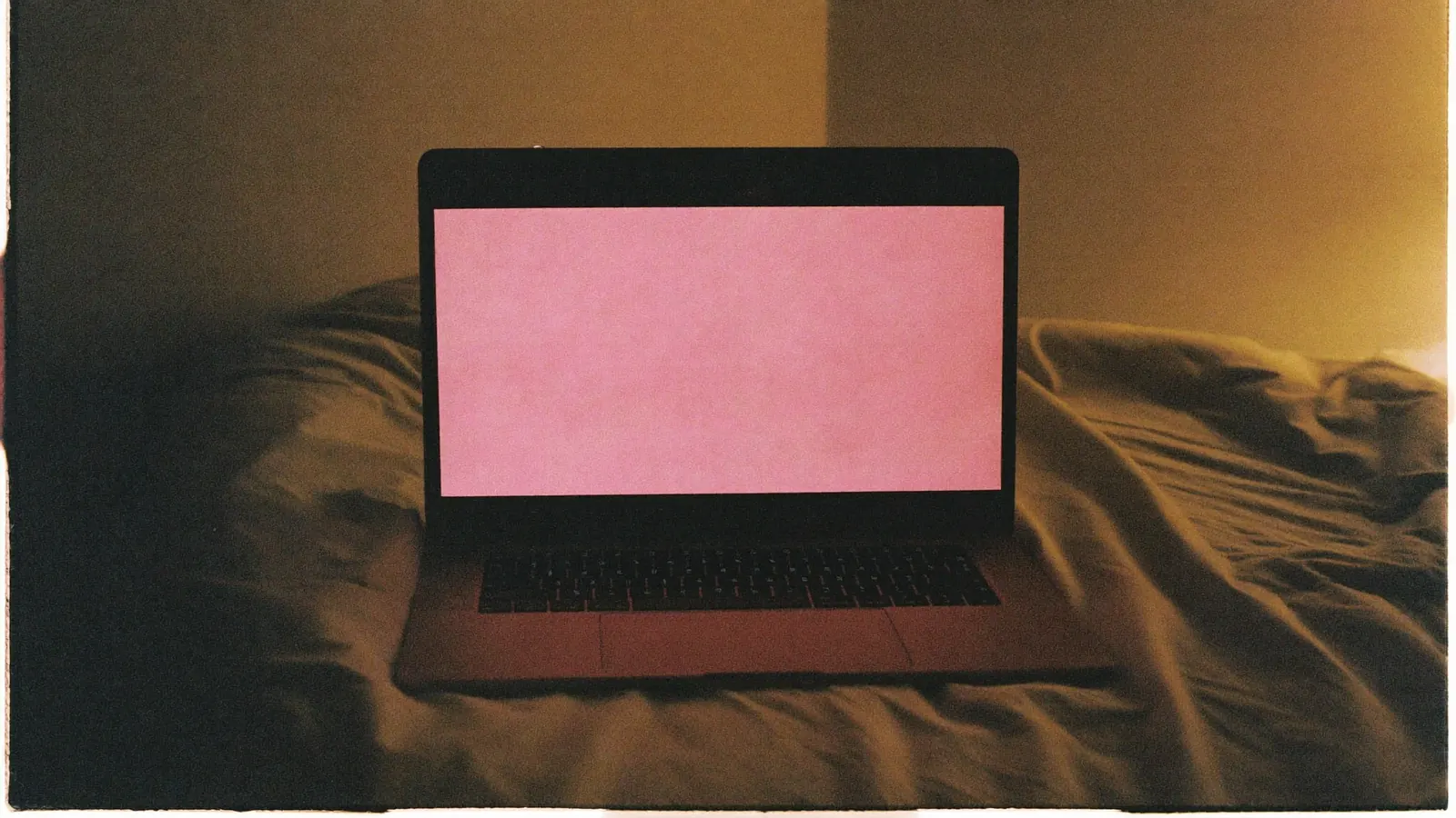 An open laptop glowing pink on a bed at night