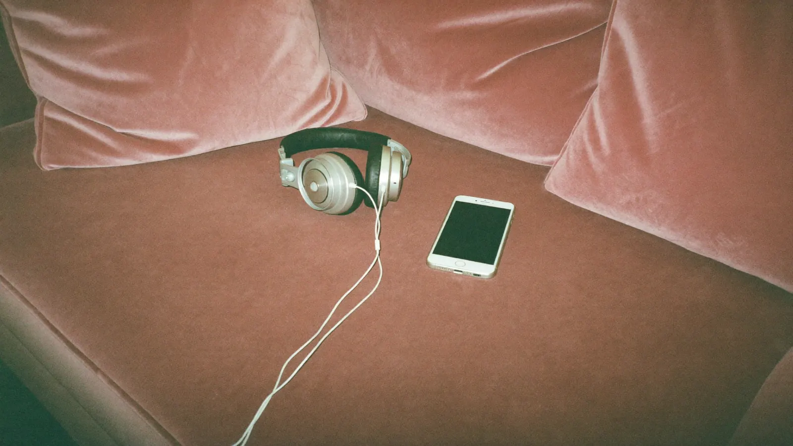Headphones and a smartphone on a pink velvet sofa