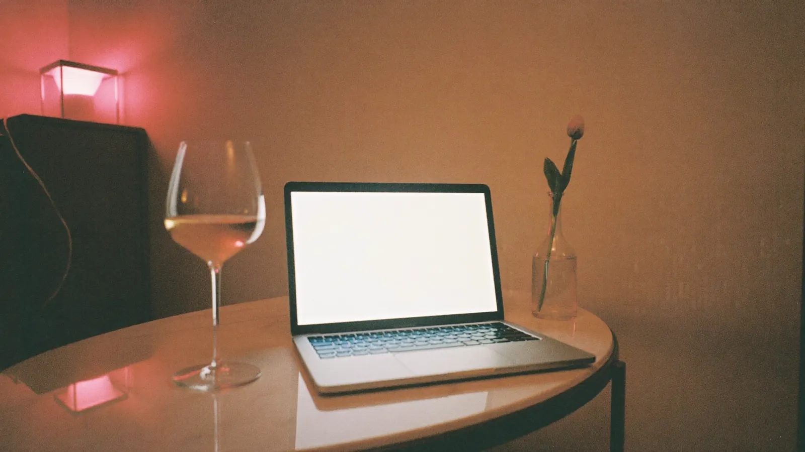 Open laptop beside a glass of rosé on a side table at dusk