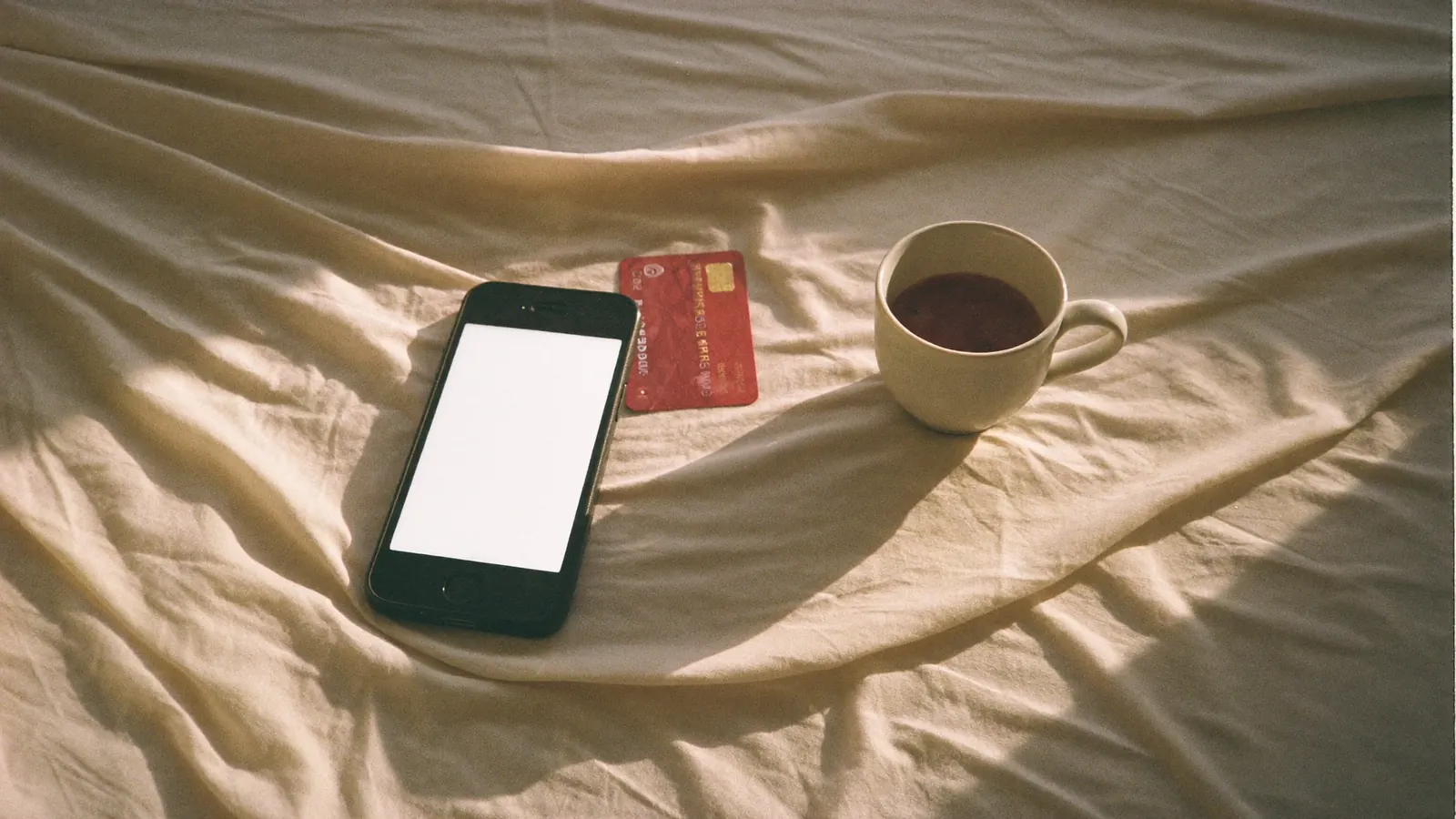 Phone and a bank card on linen sheets in morning light