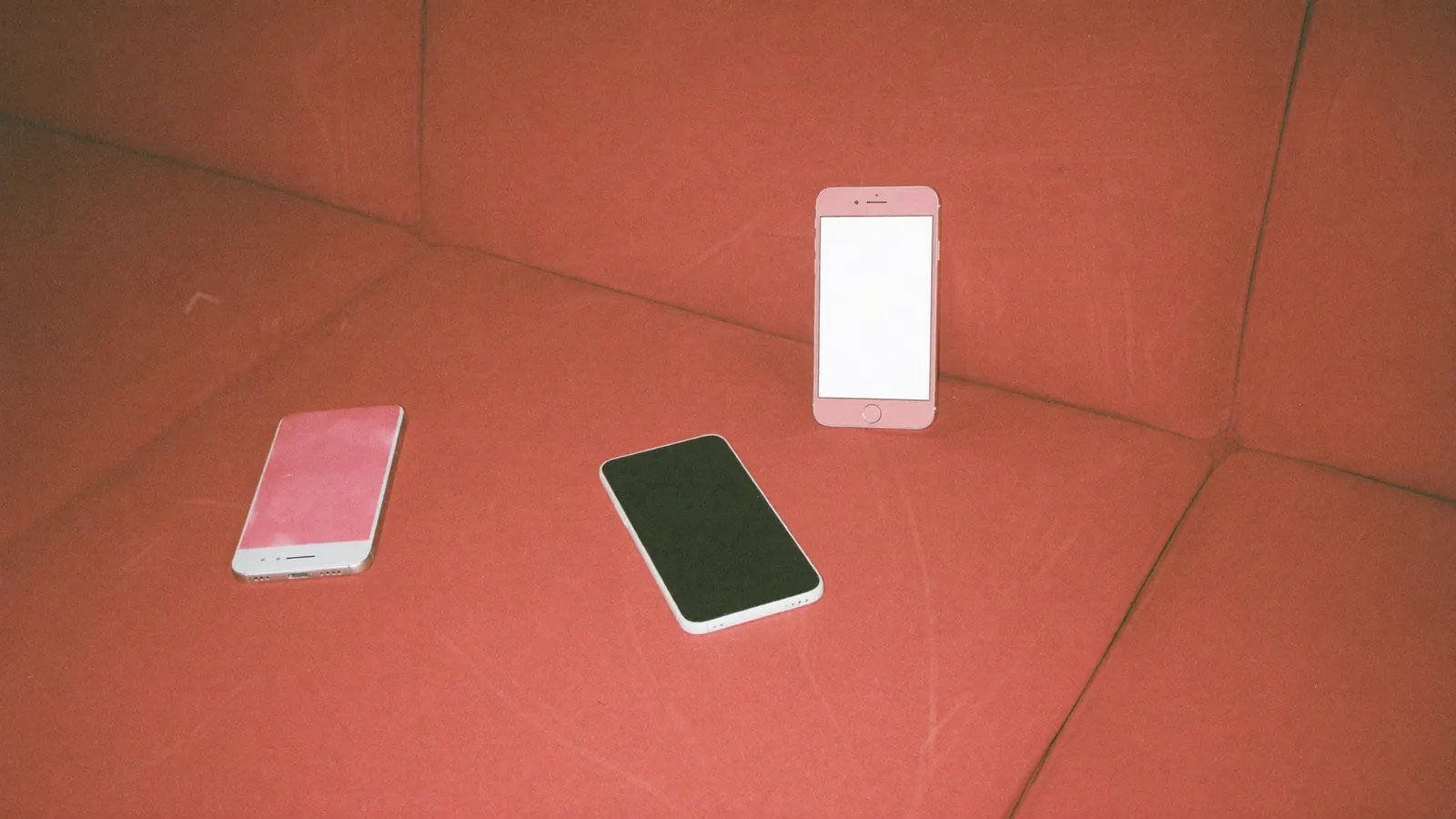 Two phones side by side on a red velvet sofa cushion