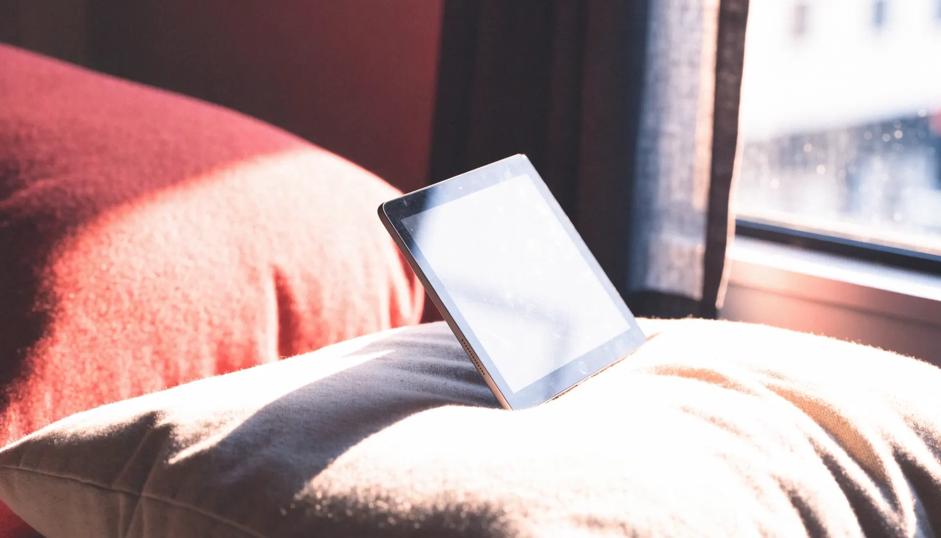 A tablet propped against cushions by a window